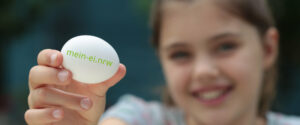 Foto: Mädchen präsentiert Ei mit Aufdruck mein-ei.nrw (Copyright: Yavuz Arslan | mein-ei.nrw)